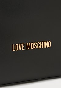 Melnā mākslīgās ādas soma ar zelta toņa "LOVE MOSCHINO" logo. Gluda tekstūra ar minimālistisku dizainu un bez papildu rotājumiem.