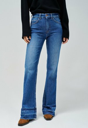 Jeans de denim azul acampanados con una cintura alta, que presentan un ligero desvanecimiento, cinco bolsillos y un acento marrón en el botón.