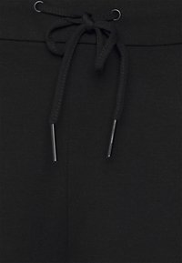 Närbild av svarta tygbyxor med knuten svart dragsko som har metallaglet och sydd midja.