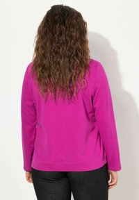 Top fucsia a maniche lunghe con scollatura rotonda, caratterizzato da una texture liscia e una vestibilità comoda. Dettagli di cucitura visibili lungo l'orlo.
