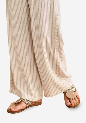 Pantalones beige de pierna ancha con finas rayas verticales combinados con sandalias marrones con tiras trenzadas y un gran detalle metálico circular.