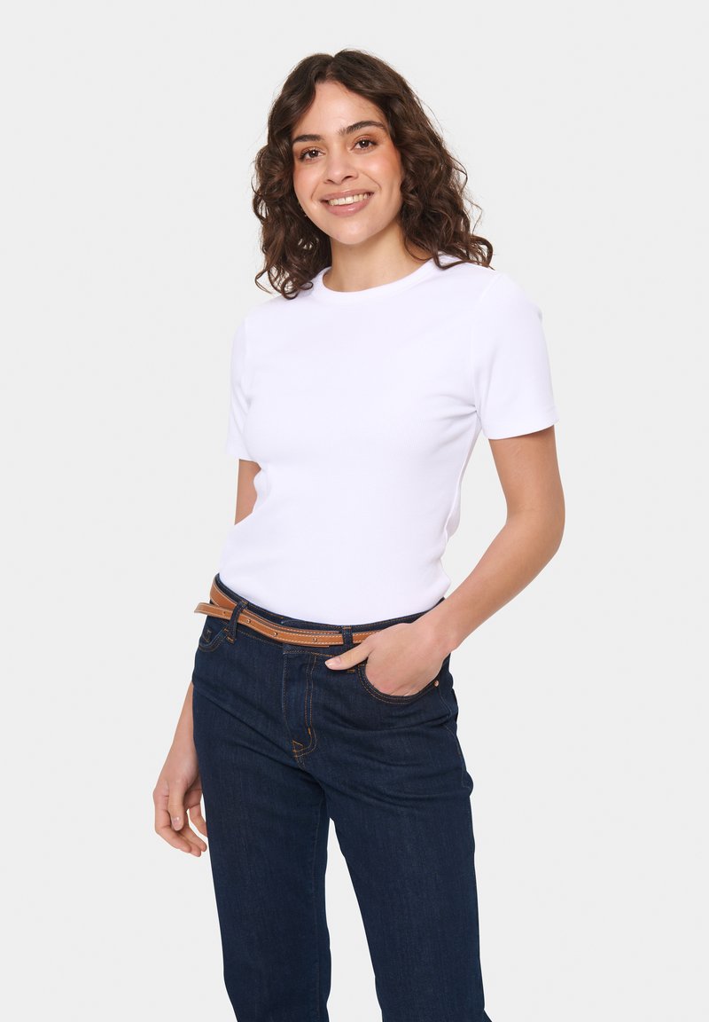 Tricou alb cu maneci scurte si decolteu rotund, purtat cu blugi denim de culoare albastru închis și o curea maro. Design minimalist și formă ajustată.
