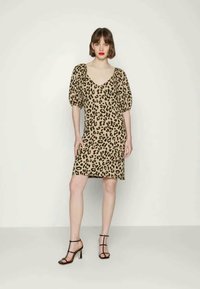Vestido de estampado de leopardo em bege com um decote em V profundo e mangas bufantes, combinado com sandálias pretas de tiras. Tecido suave, silhueta ajustada.