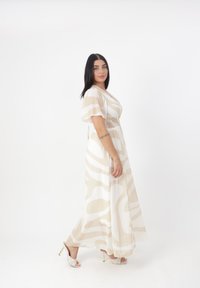 Robe maxi avec un motif abstrait beige et crème. Dotée d'un décolleté en V, de manches courtes et d'une taille smockée. Associée à des sandales à talons avec lanières.