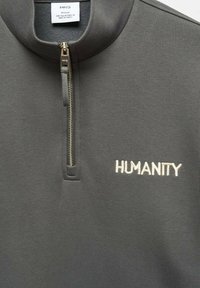 Sweat-shirt zippé gris foncé avec col montant, présentant un broderie "HUMANITY" en beige clair et un détail de fermeture éclair métallique.