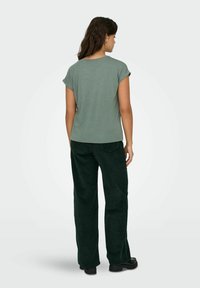 T-shirt verde a maniche corte con fit rilassato, abbinato a pantaloni larghi in corduroy verde scuro. Tessuto testurizzato dall'aspetto morbido.