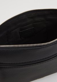 Bolso de cuero negro con un exterior texturizado, cierre de cremallera plateado y forro de tela suave. Cuenta con un bolsillo interior con una etiqueta.