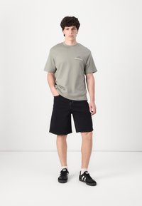 Grå bomulds-t-shirt med "ATHLETIC CLUB" print, parret med sorte denimshorts og sorte sneakers med hvide detaljer.