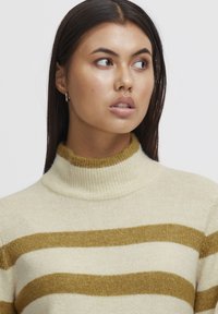 Strickrollkragenpullover in Creme mit kräftigen goldenen Streifen. Weiche Textur mit geripptem Kragen und Bündchen. Klassisches, lässiges Design.