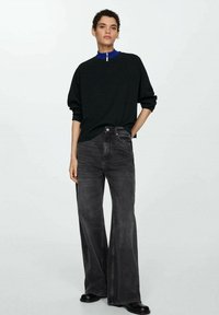 Crni oversized pulover s visokim ovratnikom i detaljem sa zatvaračem, uparen s širokim hlačama od ugljen crnogjevika i crnim čizmama do gležnjeva.