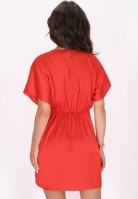 Rochie roșie, scurtă, din satin, cu o croială lejeră, mâneci scurte și un brâu elastic, având o textură netedă și un design simplu.