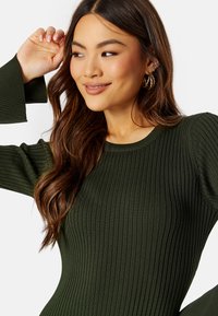 Maglione a coste verde oliva, con maniche lunghe e scollatura rotonda. Presenta una finitura testurizzata e una silhouette aderente, che esalta le forme.