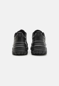 Black athletic shoes featuring a thick rubber sole, textured midsole, and mesh panels. The back has a loop and branding detail.