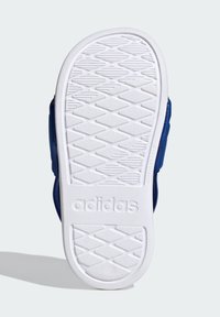 Podplat čevlja Adidas z teksturirano belo gumijasto površino, ki ima geometrijski vzorec in blagovno znamko. Nad podplatom je viden zgornji del iz mornarsko modrega materiala.