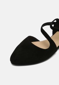 Svarta mocka ballerina skor med spetsig tå och utskurna sidor. Har ett tunt korskorsat ankelsnöre. Slät inredning.