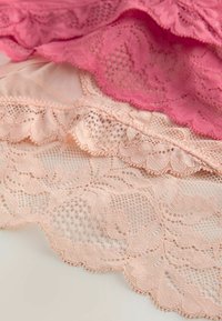 Kihtides roosa ja virsiku pitsikangas lillemotiivide ja laineliste äärtega neutraalsel taustal.