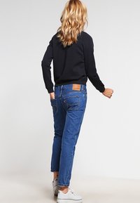 Blue denim jeans with straight legs, back pockets featuring stitching details, paired with a black long-sleeve top and white sneakers.