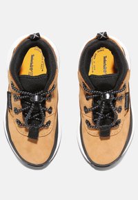 Hnědé semišové sportovní boty s černými akcenty, které mají strukturovaný svršek, elastické tkaničky a bílou gumovou podrážku.