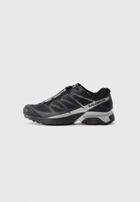 Black athletic shoe with a textured upper, reflective silver accents, and a lacing system. Designed for outdoor performance and traction.