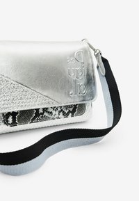 Srebrna torebka na ramię z teksturowanymi akcentami w wzór węża, wyposażona w magnetyczną klapę, tłoczone logo oraz dwukolorowy pasek w czerni i szarości.