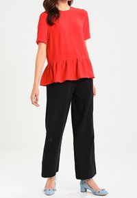 Rode peplumtop met korte mouwen, gecombineerd met zwarte wijde broek. Lichtblauwe hakken hebben decoratieve accenten op de tenen.