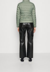 Puchowa, jasnozielona kurtka z wysoką kołnierzem; czarne skórzane spodnie o szerokich nogawkach; czarne buty z białymi podeszwami; gładkie tekstury.