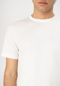 T-shirt bianco in cotone a maniche corte, con un sottile logo in rilievo "Blauer USA" sul davanti. Collo a giro semplice.