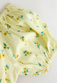 Gult stof med et blomsterprint bestående af små, spredte gule blomster og grønne blade; elastikindsat kant.