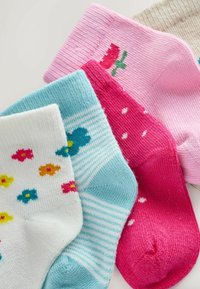 Neljä värikästä vauvasukkaa: valkoinen kukkakuviolla, sininen raidallinen perhosella, vaaleanpunainen pilkuilla ja vaaleanpunainen tulppaanikuviolla.