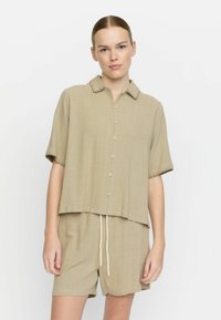 Beige short-sleeve button-up shirt with a collar and decorative stitch detailing, paired with matching shorts featuring an elastic waistband.