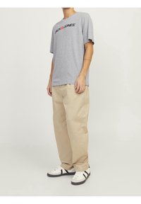 Šedé tričko s černým logem "JACK & JONES", spárované s béžovými volnými kalhotami a bílými teniskami s černými akcenty.