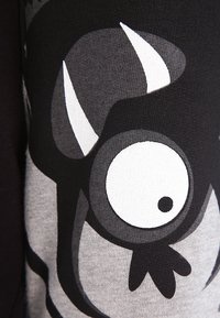 Zwarte en grijze stof heeft een ontwerp van een cartoonmonster met een groot oog en hoorns. De textuur is zacht en rekbaar.