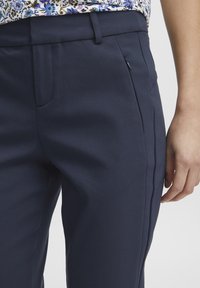 Marineblauwe op maat gemaakte broek met een zachte textuur, zijzakken en een elegant ontwerp. Beschikt over een tailleband en subtiele plooien aan de voorkant.