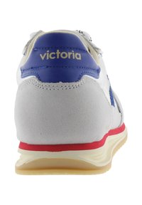 Vista trasera de una zapatilla blanca con talón de ante gris, parte superior de cuero azul con el texto "victoria", franja roja en la entresuela y suela beige.