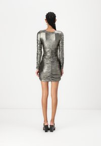 Robe mini en argent métallique avec de longues manches froncées, silhouette ajustée et finition texturée. Présente un dos dégagé et tombe au-dessus de la mi-cuisse.
