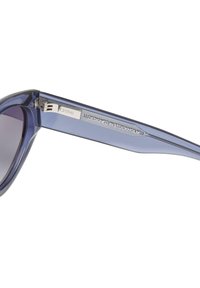 Ochelari de soare dreptunghiulari cu ramă transparentă purpurie, lentile întunecate și un accent metalic pe braț care spune "CHIMI DESIGNAT ÎN STOCKHOLM."