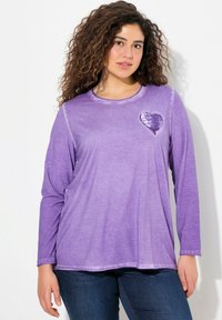 Langärmliges lila Shirt mit einem taillierten Halsausschnitt und einem mit Pailletten verzierten Herzdetail auf der Brust. Weicher Stoff mit einem lockeren Schnitt und leichtem Glanz.
