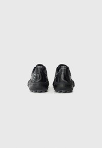 Une paire de chaussures de sport noires avec une semelle texturée et des languettes de tirage, présentées de dos sur un fond clair.