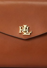 Brun läderhandväska med ett guldlogo-spänne och en kuvert-stil lucka. Har rena linjer och en slät yta, med kontrasterande sömmar.