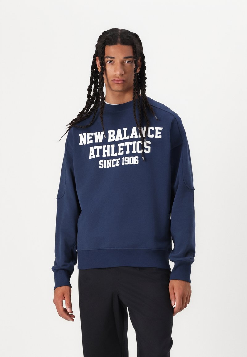 Tengerészkék pulóver, amelyen fehér szöveg olvasható: "New Balance Athletics Since 1906" az elején. Bordás mandzsetták és alsó szegély, laza fazon, puha anyagú textúra.