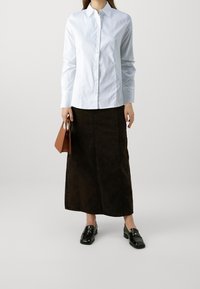 Biała koszula z wykładanym kołnierzykiem, zestawiona z brązową dżinsową spódnicą maxi i czarnymi loafersami. Dodatki to brązowa torebka.