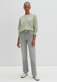 Maglione verde chiaro con una vestibilità rilassata, jeans dritti grigi e scarpe bianche senza lacci. Tessuto morbido e design minimalista.