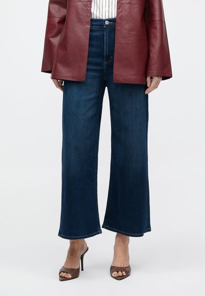 Sötétkék farmer széles szárú nadrág magas derékkal, befejezett szegélyekkel és finom kopással, bordó bőrdzsekivel párosítva.