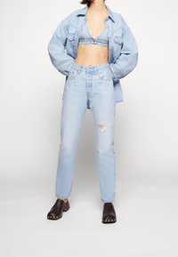 Ljusblå denimjacka, matchande denimbralett, högmidjade ljusblåjeans med slitdetaljer och mörkbruna träskor.