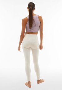 Leggings leggeri e a vita alta di colore crema, con una texture liscia, due tasche posteriori e una vestibilità aderente alla caviglia. Top corto di colore lilla.
