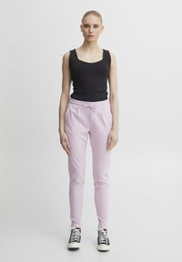 Svart ribbad tanktop kombinerad med ljusrosa joggerbyxor med dragsko i midjan; modellen har på sig svarta och vita sneakers.