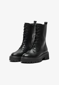 Et par svarte lær ankelstøvler med snøring, sidesk zipper og tykke såler på en hvit bakgrunn.