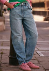 Jeans de denim azul claro con un ajuste relajado, diseño de cinco bolsillos y un desvanecimiento sutil. Combinados con zapatillas de ante rosa suave.