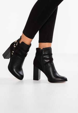 Botas negras hasta el tobillo hechas de cuero liso y ante, con un tacón cuadrado, cremallera lateral y correas con detalles de metal.