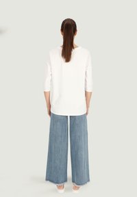 Biała bluzka z trzema czwartymi rękawami w połączeniu z szerokimi, jasnoniebieskimi dżinsami o surowym wykończeniu i luźnym kroju.